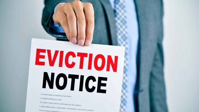 person-in-a-business-suit-holding-up-a-piece-of-paper-with-the-words-eviction-notice-in-bold-terms